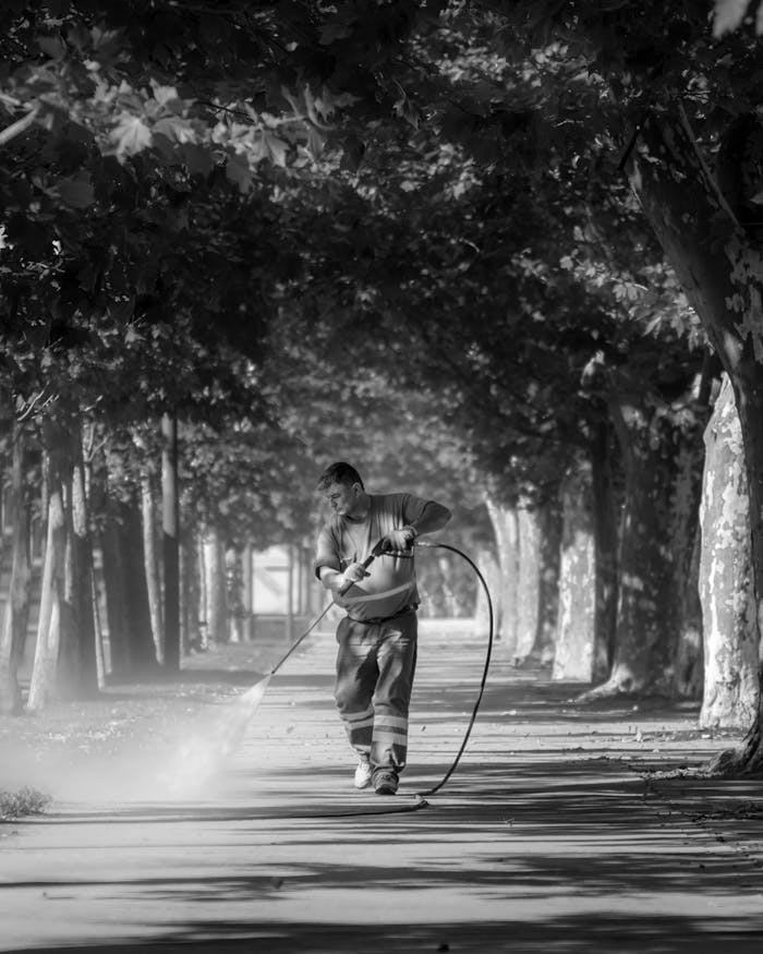 A man cleaning a city street with a hose in a black and white photograph, Buenos Aires.