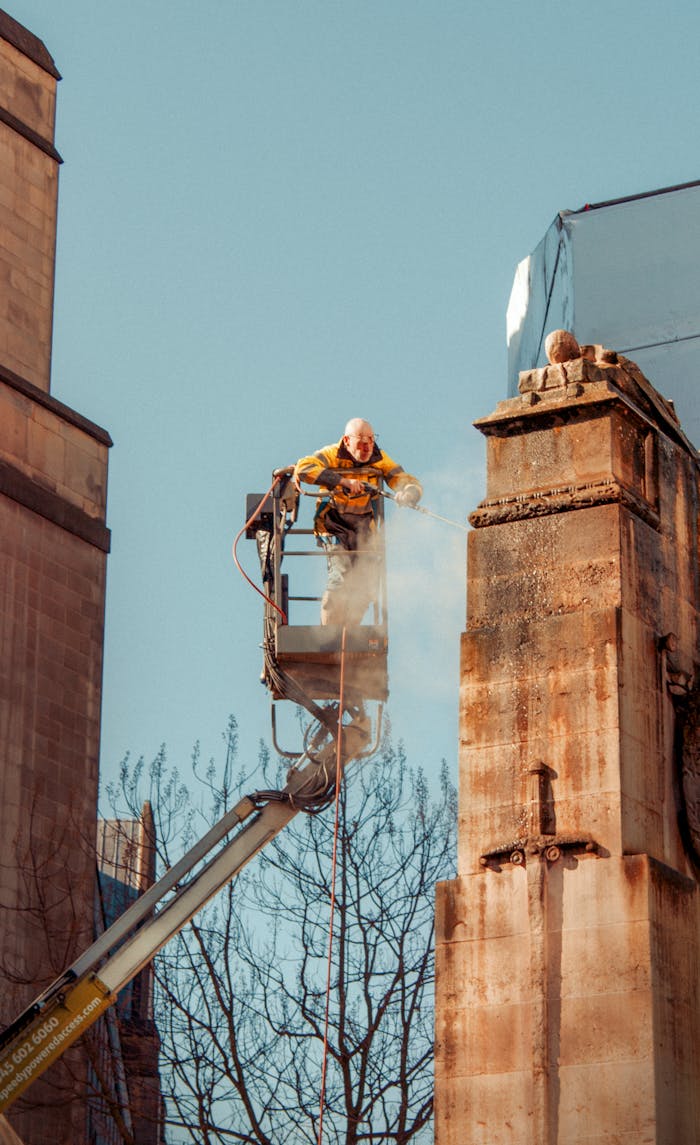 A construction worker jet washes stonework in Manchester, UK. Clear blue sky background.